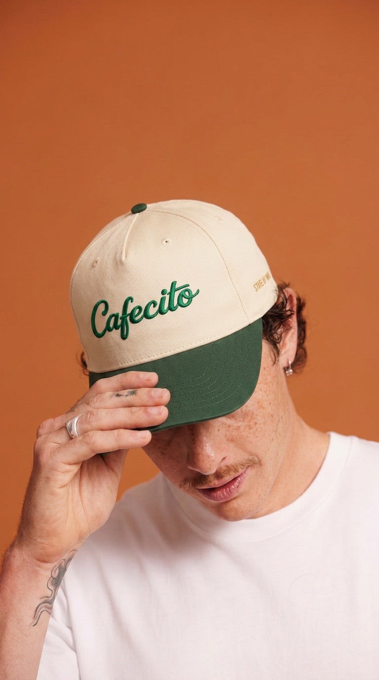 Person wearing a beige and green cap with 'Cafecito' text against an orange background
