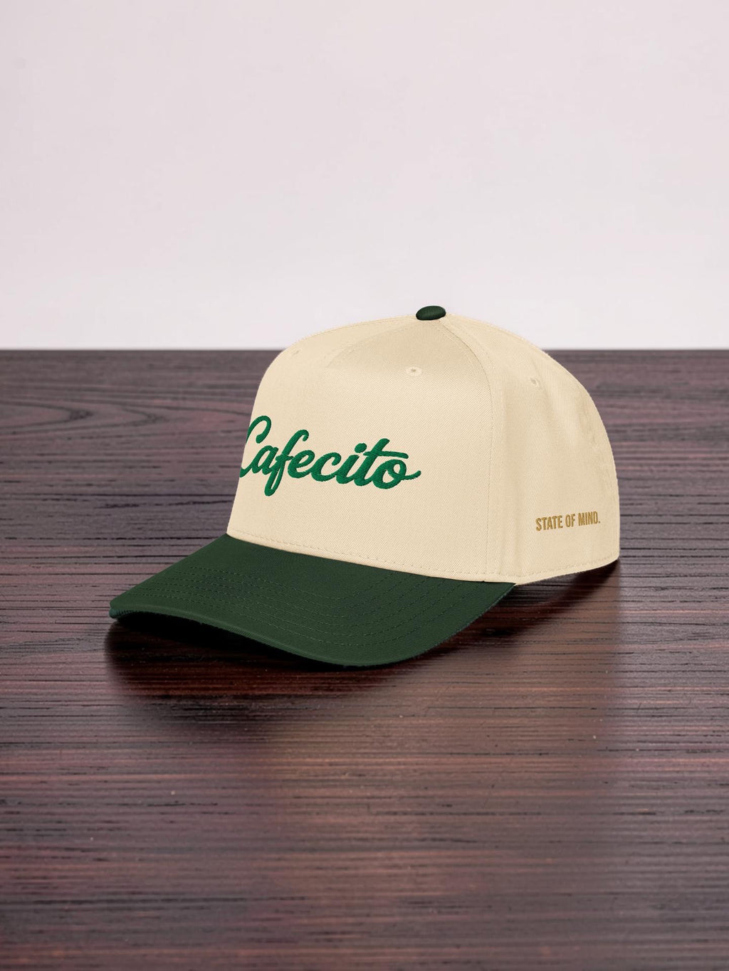 Beige and green cap with 'Cafecito' branding on a wooden surface